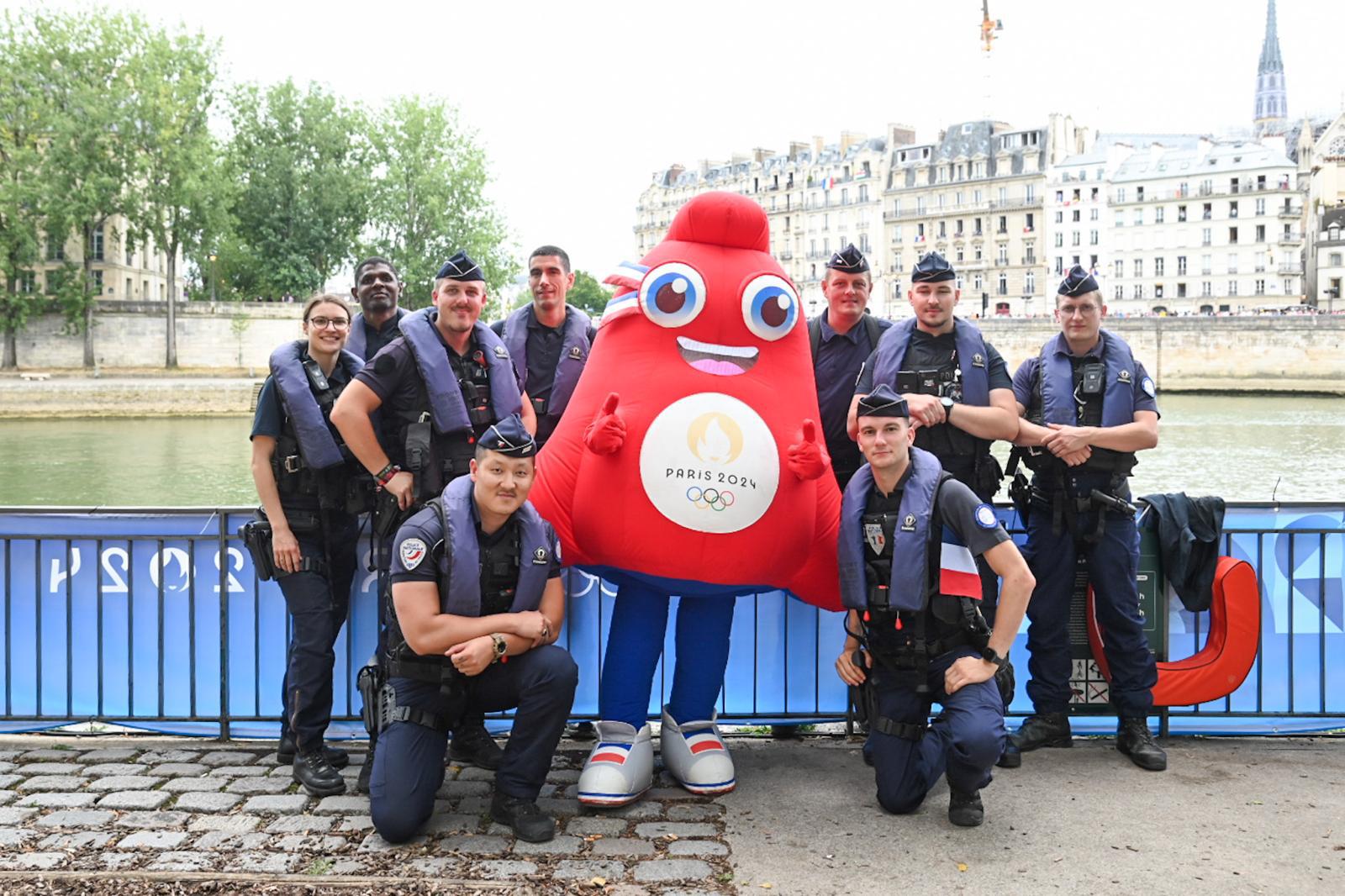 Photo de la mascotte Phryge olympique entourée par une équipe de policiers